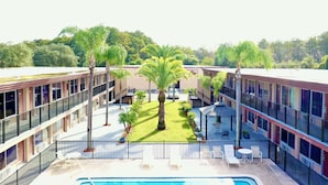 A hotel courtyard with a swimming pool, palm trees, and outdoor seating areas.