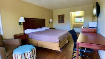 Une chambre d’hôtel avec un lit, un bureau, une chaise, une lampe, une télévision et une fenêtre.