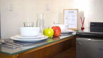 Una encimera de cocina con un refrigerador, una jarra de vidrio, un tazón, un plato, una cuchara, un tenedor y dos manzanas.