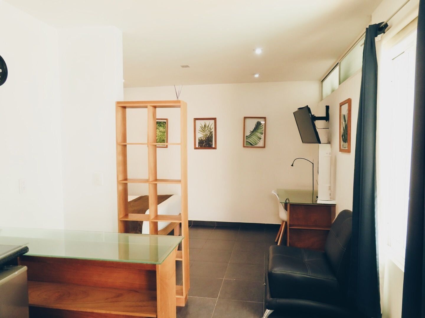 Una habitación con un escritorio de madera, una silla de cuero negro, una mesa de vidrio y una estantería.
