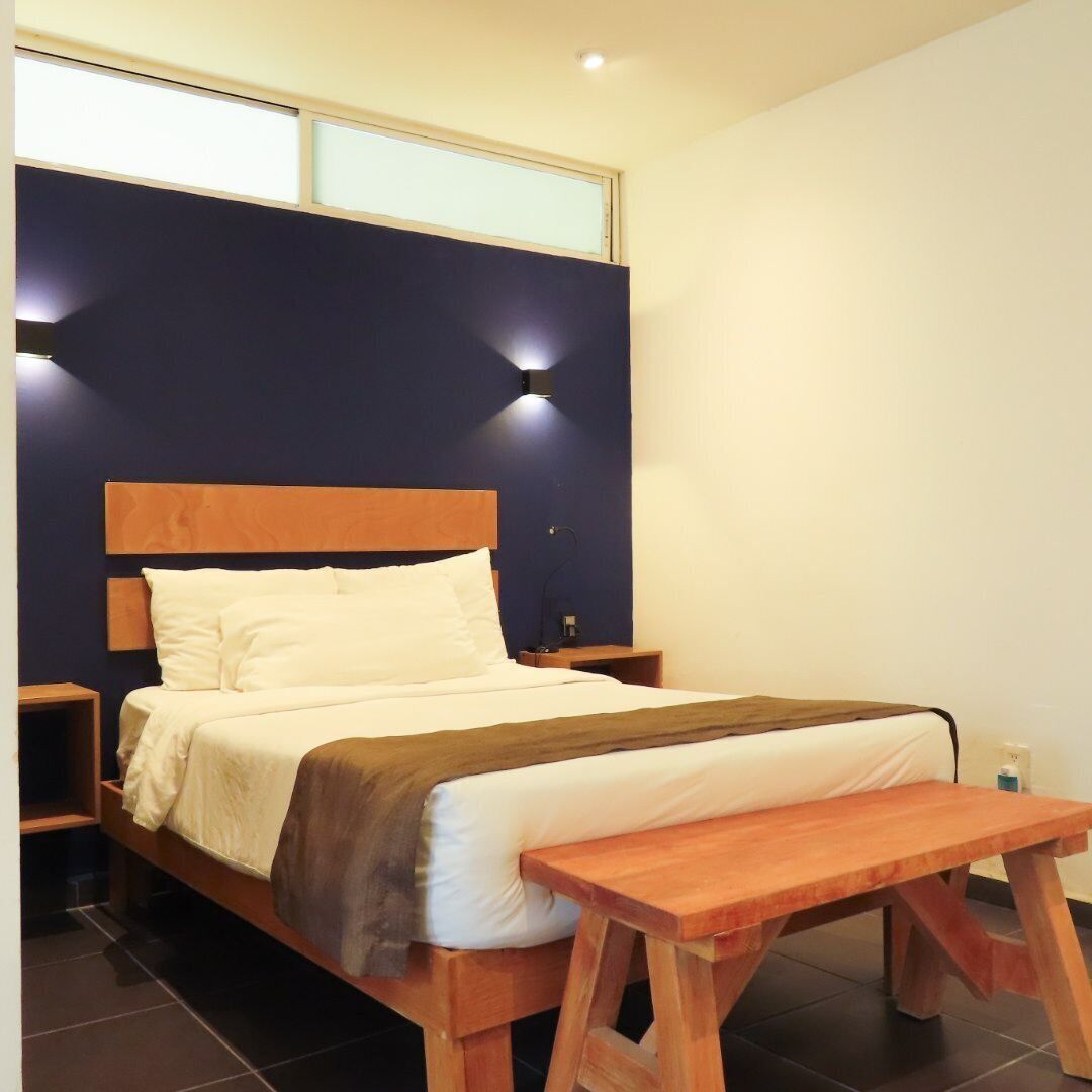 A modern bedroom with a wooden bed, bedside tables, a bench, and a wall-mounted light fixture.