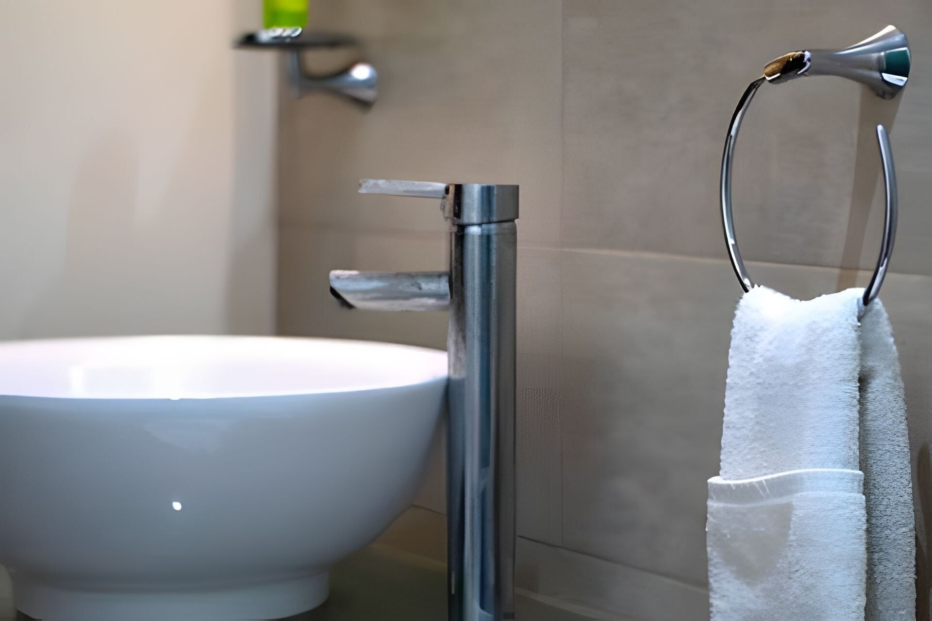 Un baño con lavamanos blanco, grifo cromado y un perchero con toalla blanca.
