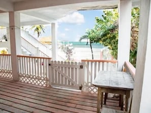 A wooden deck with a white gate, leading to a beach view with palm trees and a clear sky. - Chai's Beach House (San Pedro)