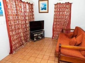 A living room with a sofa, a TV on a stand, and patterned curtains. - Chai's Beach House (San Pedro)