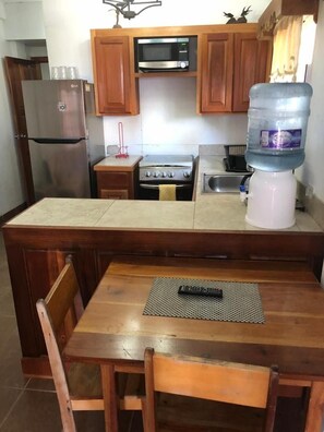 A compact kitchen with wooden cabinets, a built-in microwave, a stainless steel refrigerator, a gas stove, and a water dispenser.