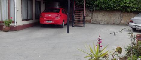 A red car parked in a garage with a wooden ladder and a red cloth hanging on the balcony.