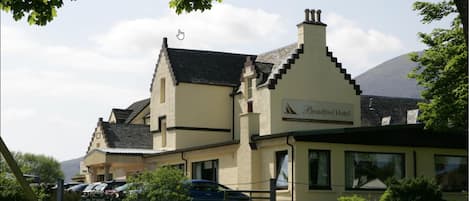 A building with a sign reading "Broadford Hotel." It has a traditional architectural style with a steeply pitched roof and a chimney. There are parked cars in front of the building.