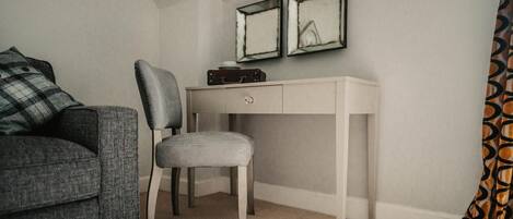 A room with a grey sofa, a grey chair, a white desk, and two framed mirrors on the wall.