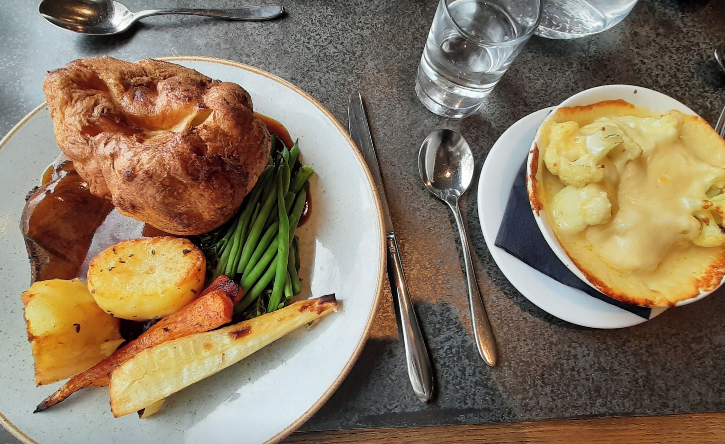 A plate with Yorkshire pudding, roasted potatoes, green beans, and gravy.