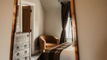 Een slaapkamer met een bed, een stoel, een dressoir en een raam met gordijnen.