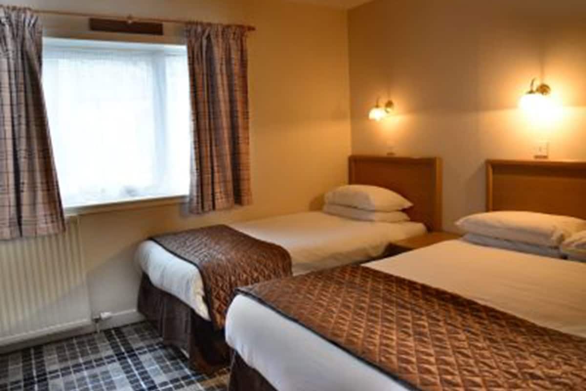 Ein Hotelzimmer mit zwei Betten, einem Fenster mit Vorhängen und zwei Wandlampen.
