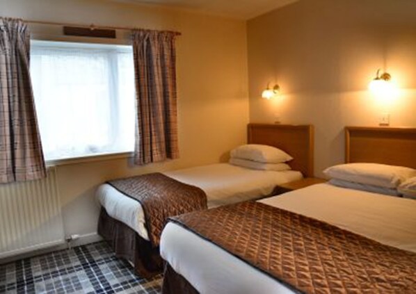 Une chambre d’hôtel avec deux lits, une fenêtre avec des rideaux et deux lampes fixées au mur.