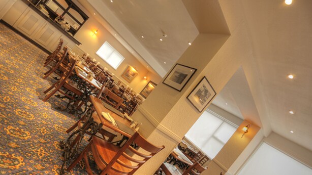 A spacious dining area with multiple tables and chairs, a patterned carpet, and framed artwork on the walls. - Tongadale Hotel (Portree)