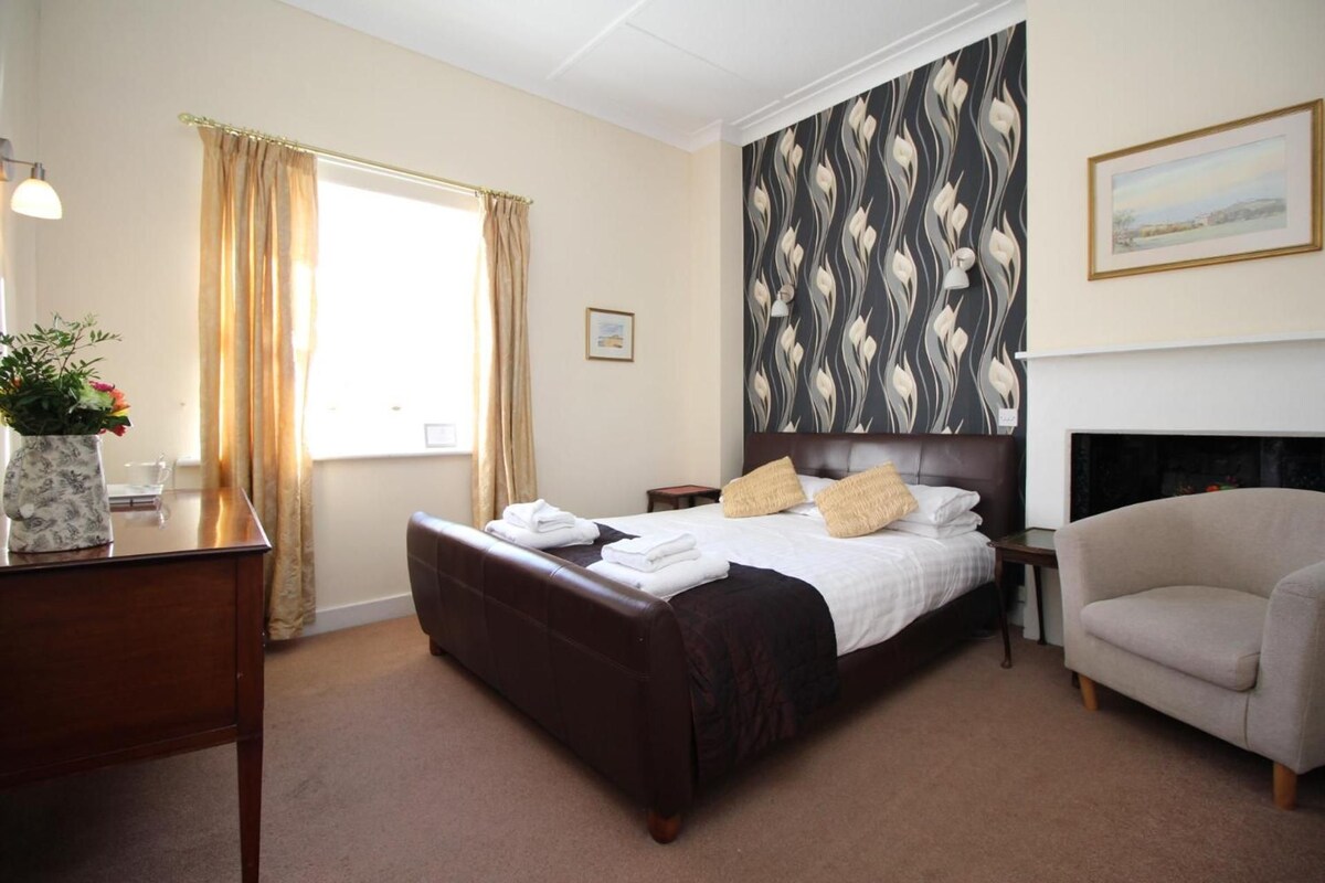 A hotel room with a bed, a chair, a desk with a lamp, and a window with curtains.