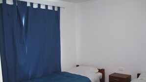 Una habitación pequeña y sencilla con dos camas individuales, una mesita de noche de madera y una cortina azul.