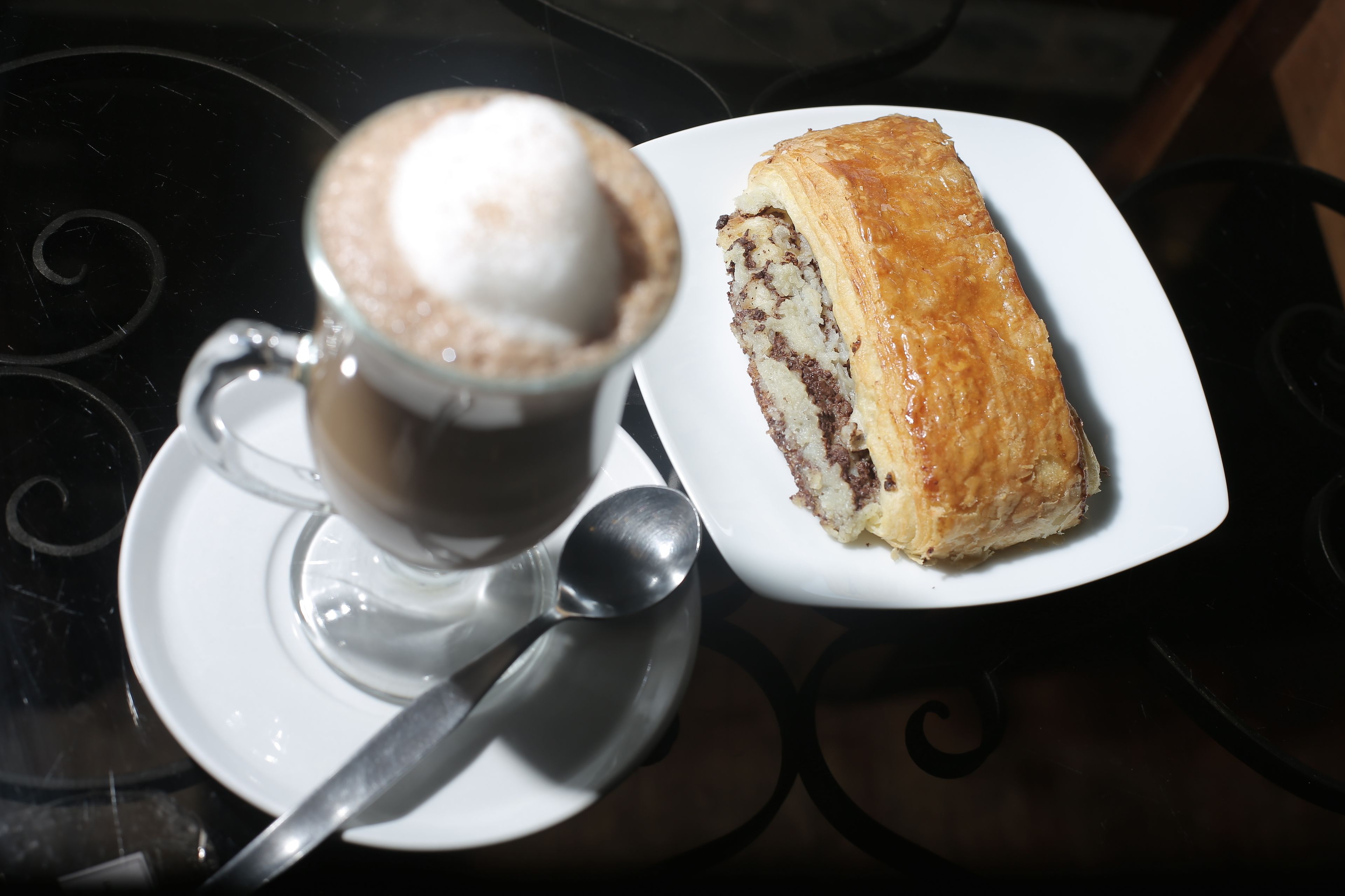 A cup of coffee with a frothy top and a pastry on a white plate.