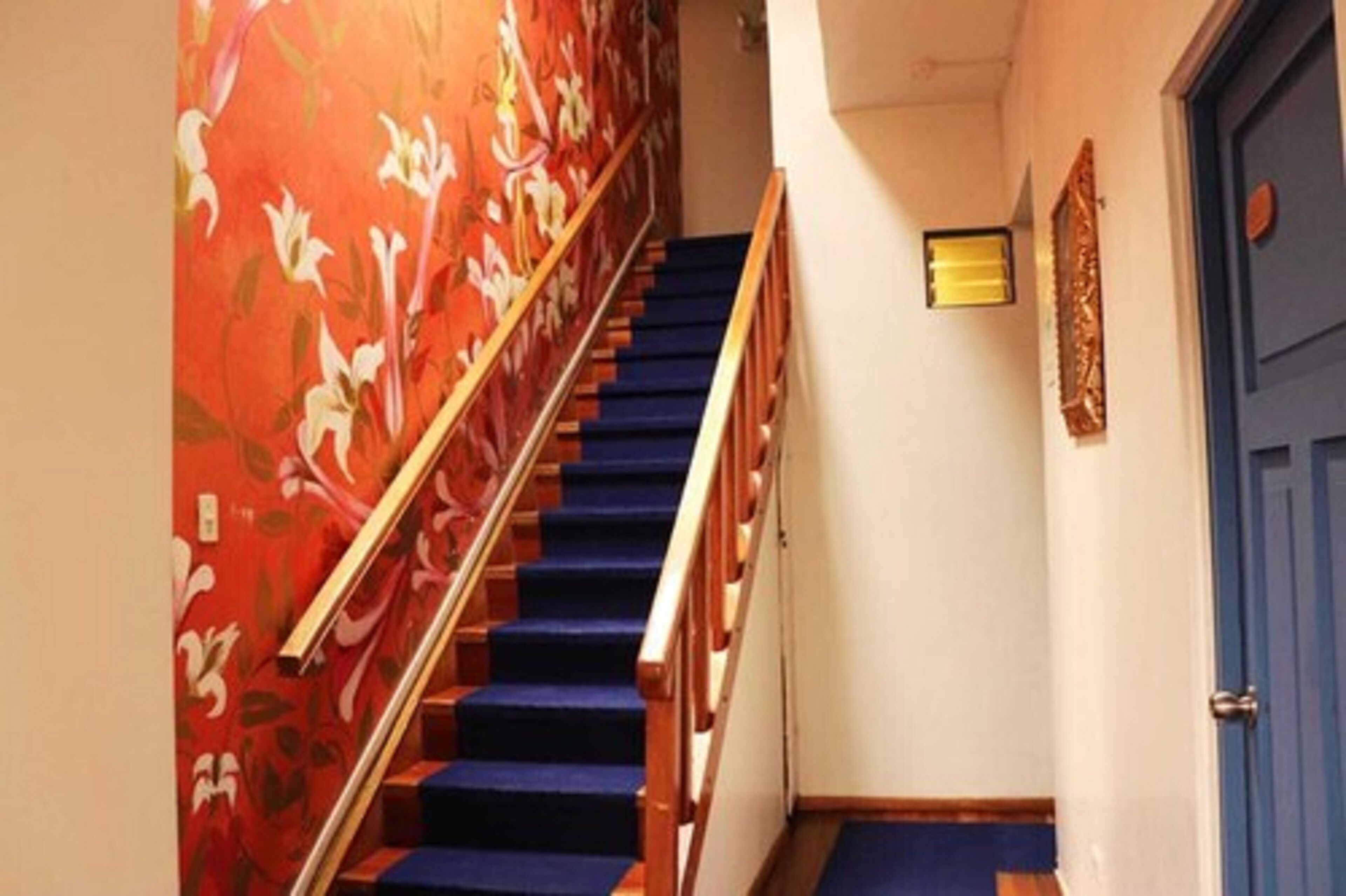 Un escalier dont les marches sont recouvertes d’une moquette bleue et qui possède une rampe en bois, menant à une pièce dont la porte est bleue.