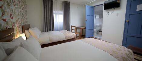 Habitación de hotel con dos camas, un escritorio, una silla, un televisor y un baño visible a través de una puerta abierta.