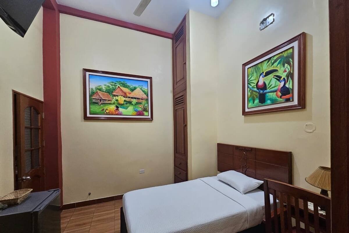 Un dormitorio con cama, cabecera de madera, mesita de noche, lámpara y dos cuadros en la pared.