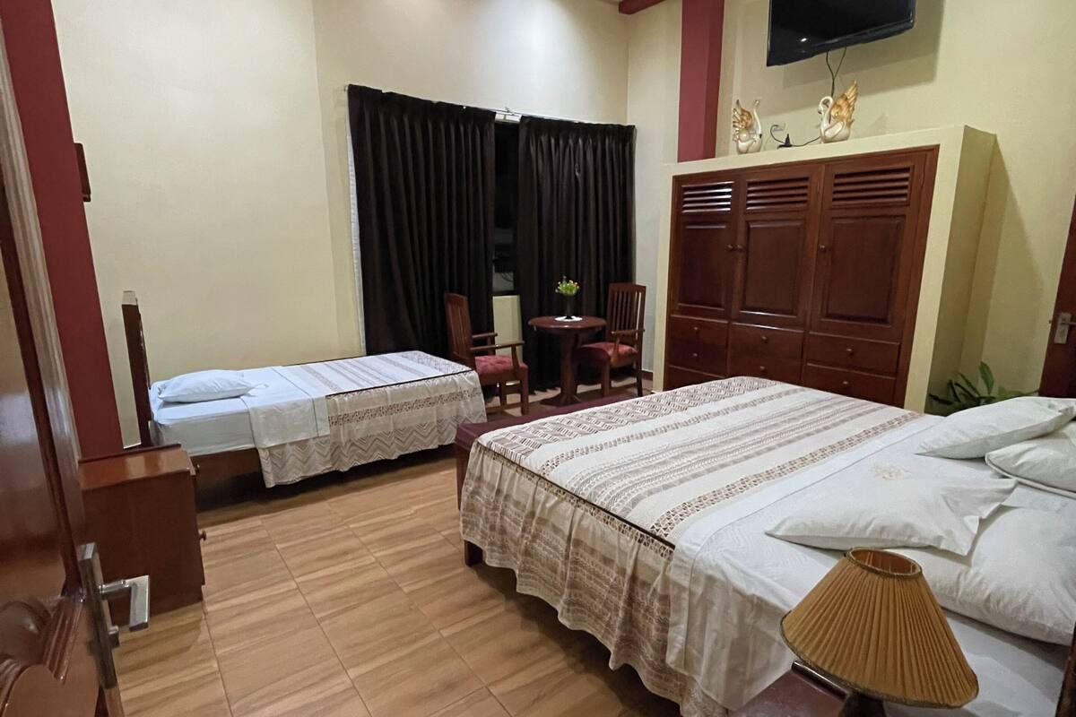 Habitación de hotel con dos camas, ventilador de techo, televisor y armario de madera.