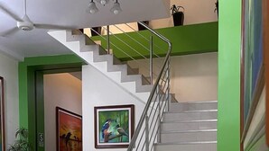 Una escalera con barandilla de metal, un ventilador de techo y una araña. Hay plantas en macetas y obras de arte enmarcadas en las paredes.