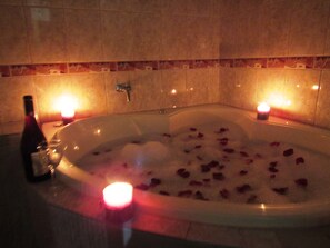 A hot tub with rose petals, candles, and a bottle of wine.