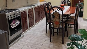 Una cocina con estufa, horno y armarios, una mesa de comedor con sillas y un ventilador de techo.