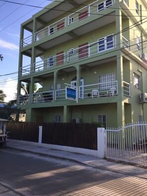 A multi-story building with balconies, a wooden fence, and a paved street.