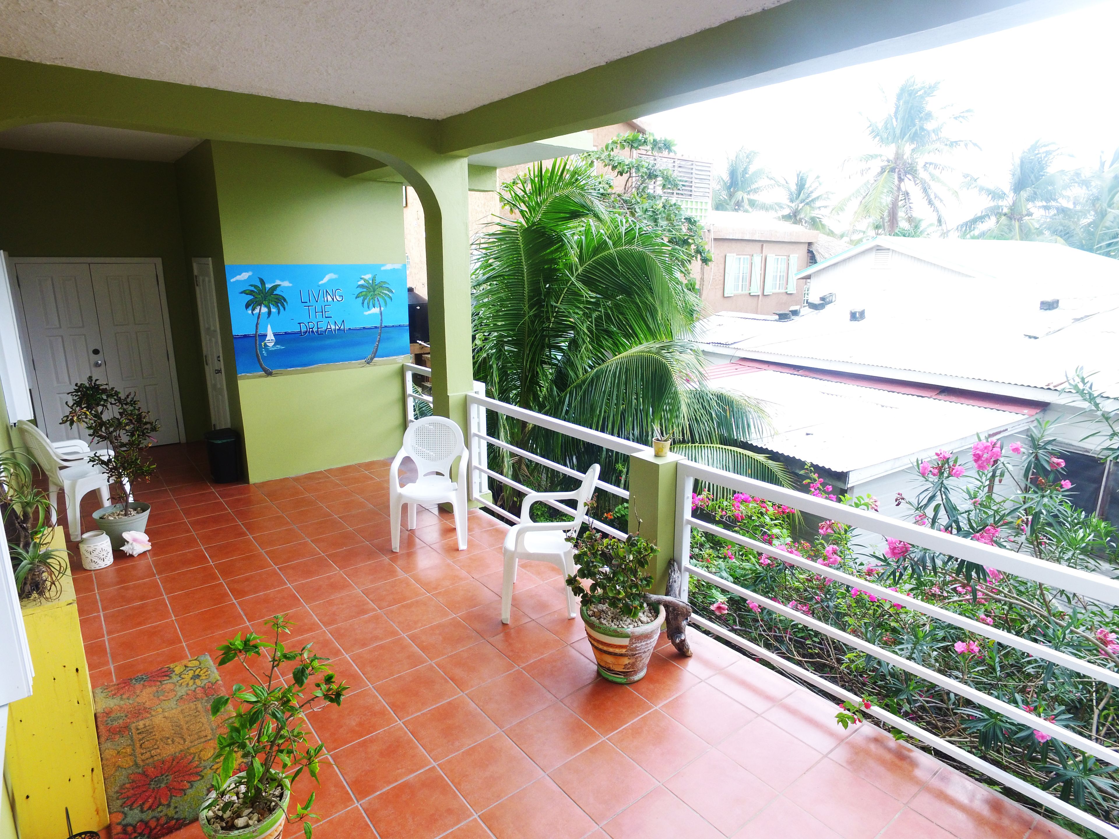 A balcony with a view of a beach mural, potted plants, and a railing.