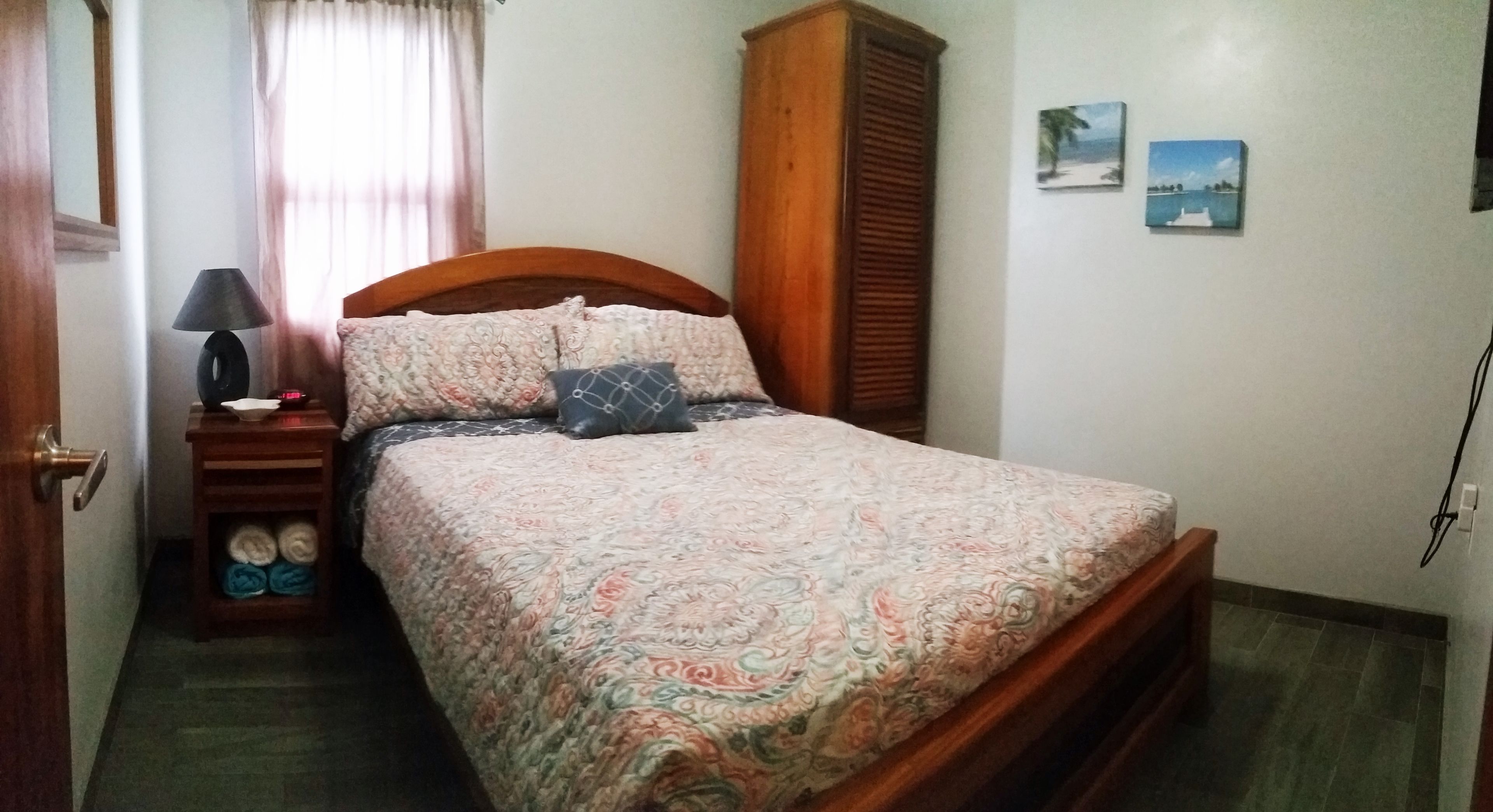 A bedroom with a bed, a nightstand, a lamp, a wardrobe, and two wall art pieces.