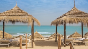 Una playa con sombrillas de paja, sillas reclinables, una terraza de madera y vista al océano.