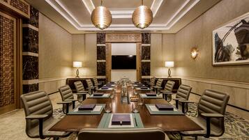 Una sala de conferencias con una larga mesa, varias sillas, dos lámparas y una pantalla grande.