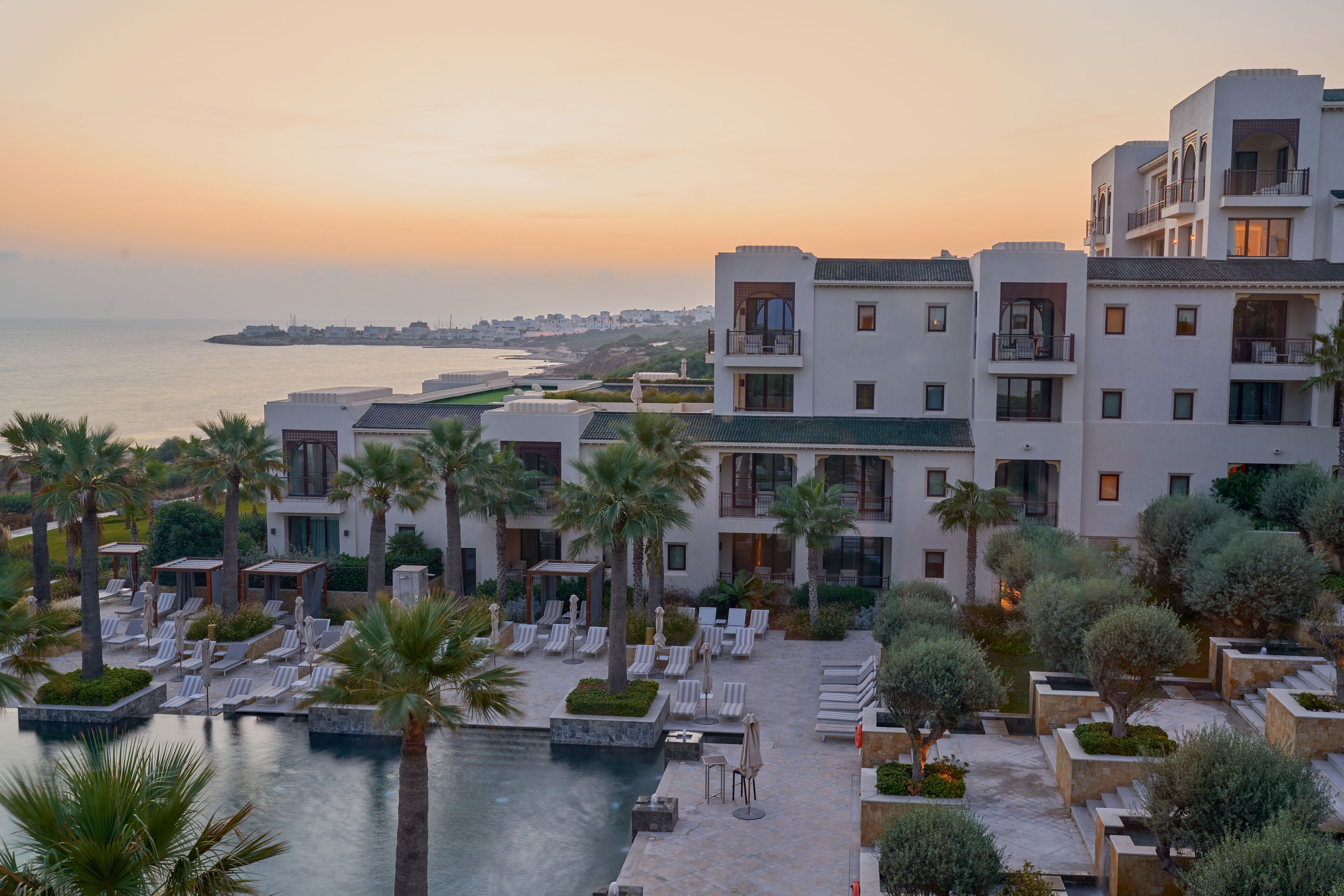 A resort with a pool, lounge chairs, and a view of the sea.