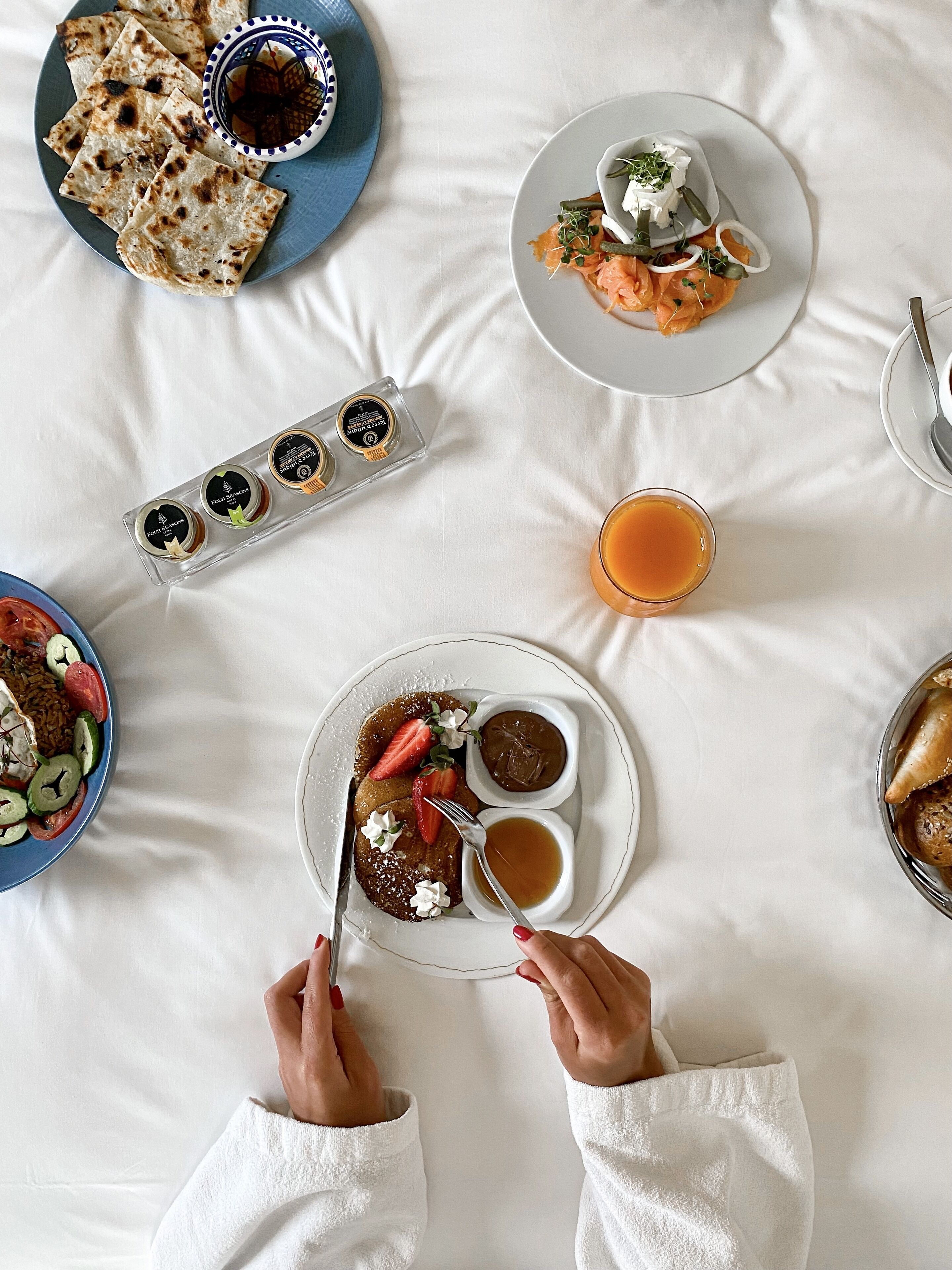 Un desayuno con diversos platos, como panqueques, salmón ahumado y pasteles, sobre un mantel blanco.