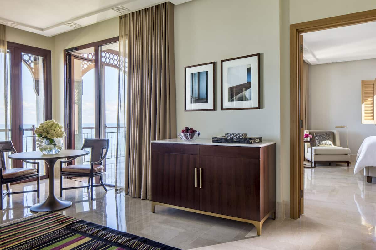 Quarto de hotel com varanda, área de refeições, cama e escrivaninha.