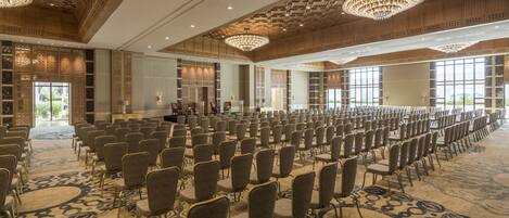 A large conference room with rows of chairs, a stage, and ornate chandeliers.