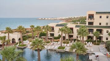 Un resort con piscina rodeada de palmeras y sillas de descanso, con vista al mar.