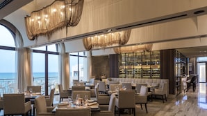 Un restaurante moderno con vista al océano, que cuenta con candelabros elegantes, asientos cómodos y una barra bien surtida.