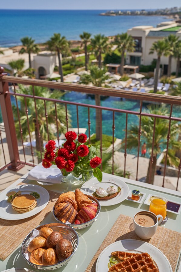 A balcony with breakfast items, a vase of flowers, and a view of the ocean and resort buildings. - Four Seasons Hotel Tunis (La Marsa)