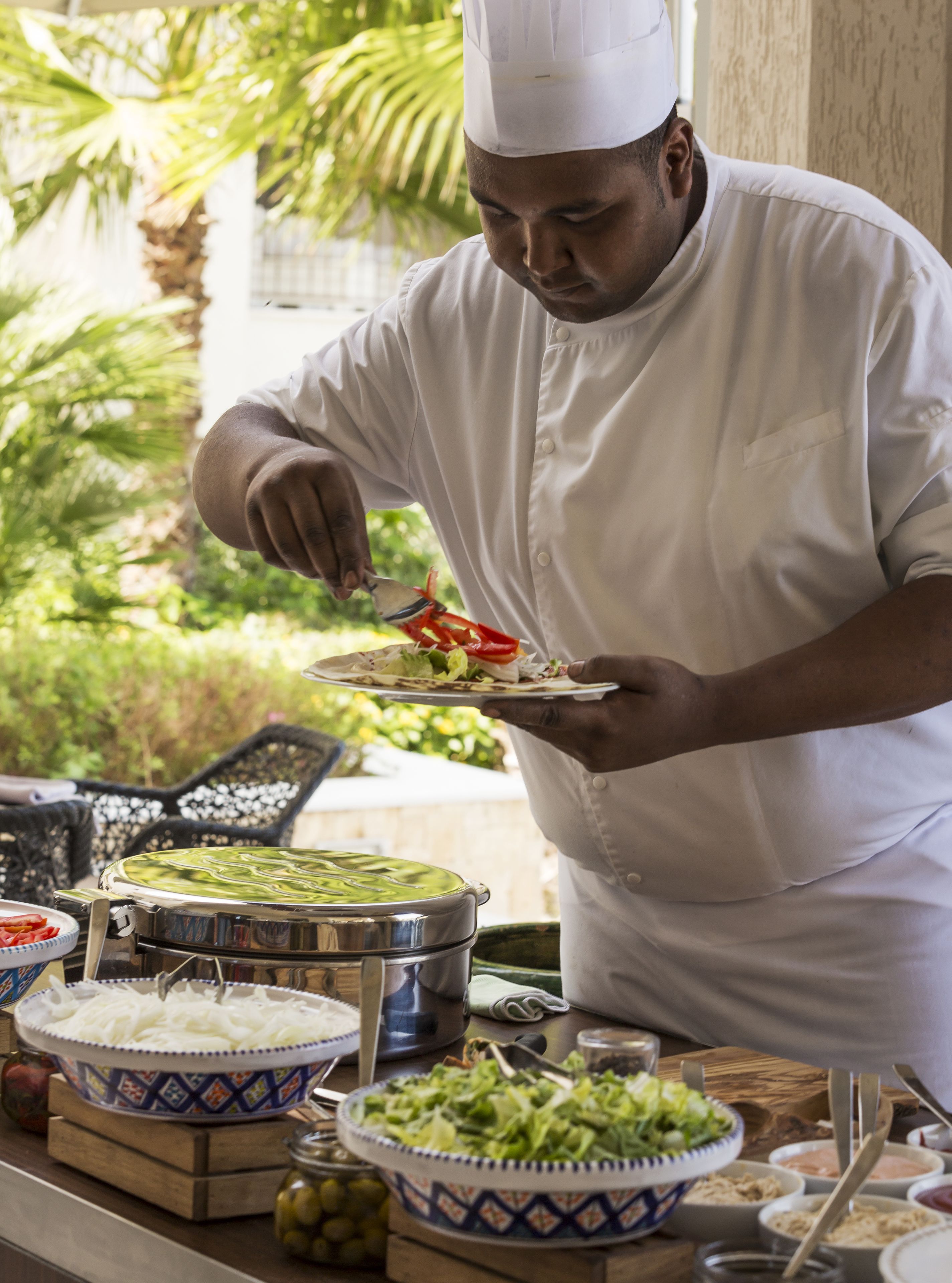 A chef preparing food outdoors with various dishes and ingredients visible.