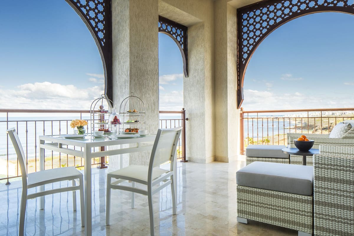 Uma varanda com mesa posta para serviço de chá, mobiliário de vime e vista para o oceano.