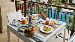 Una mesa de comedor con alimentos para el desayuno y vistas al mar y la piscina.