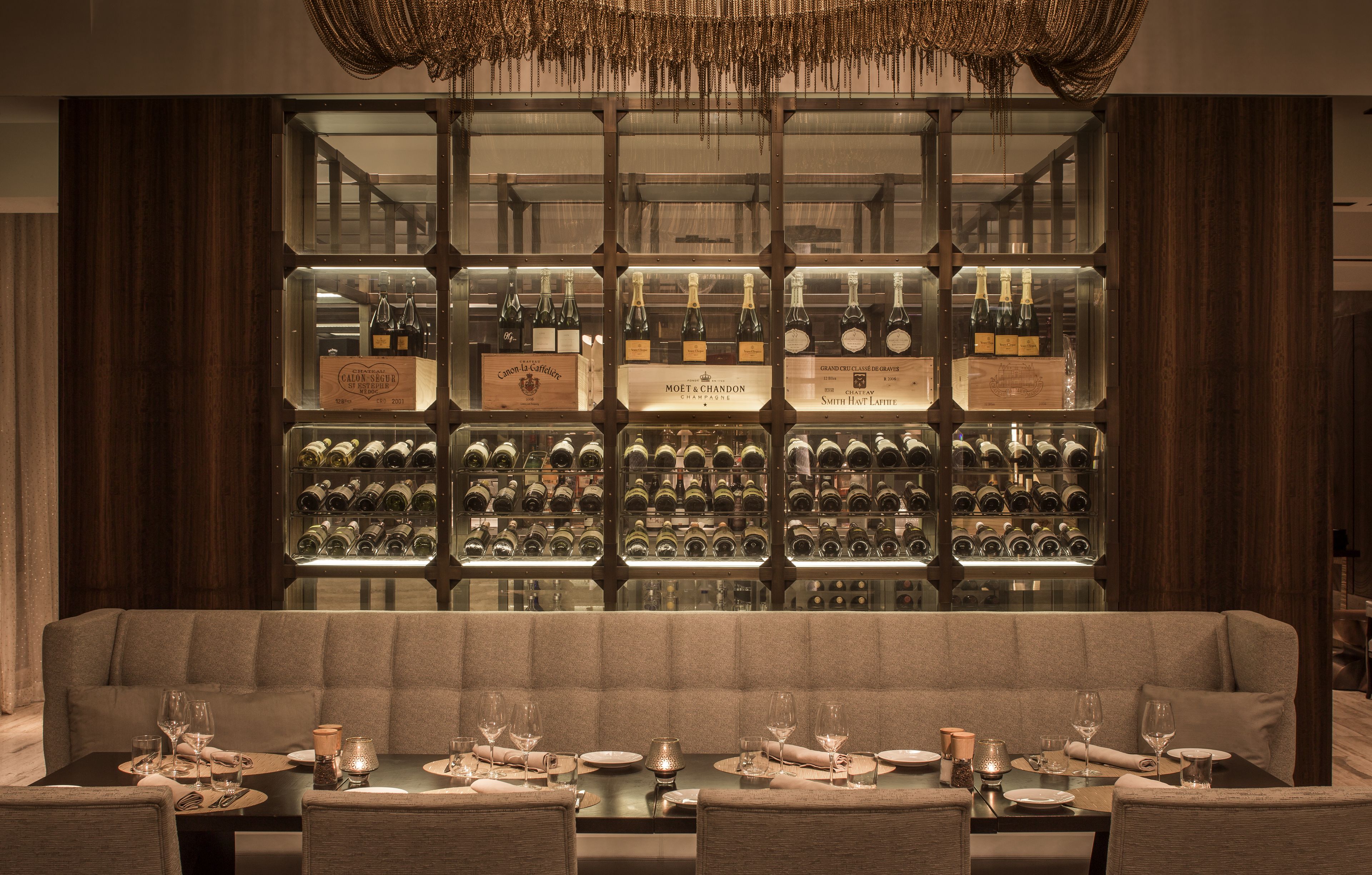 Un restaurante con una larga mesa de comedor dispuesta para una comida, una vitrina para vinos al fondo y un candelabro colgando.
