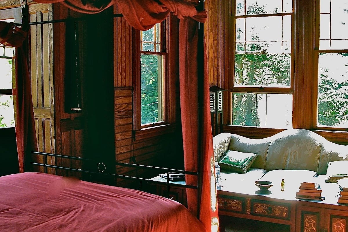 Una habitación con cama, una mesa con libros y una ventana con cortinas.