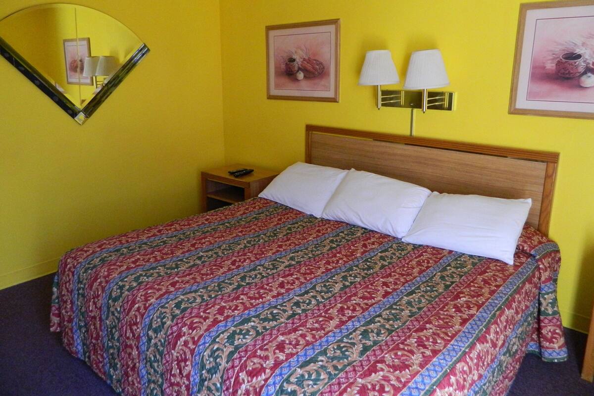 A hotel room with a bed, a nightstand, a mirror, and two wall-mounted lamps.