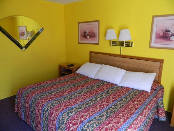 Habitación de hotel con cama, mesita de noche, espejo y dos lámparas de pared.