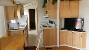 A compact kitchen with wooden cabinets, a microwave, a stove, and a television. - Marine Motel (Ajo)