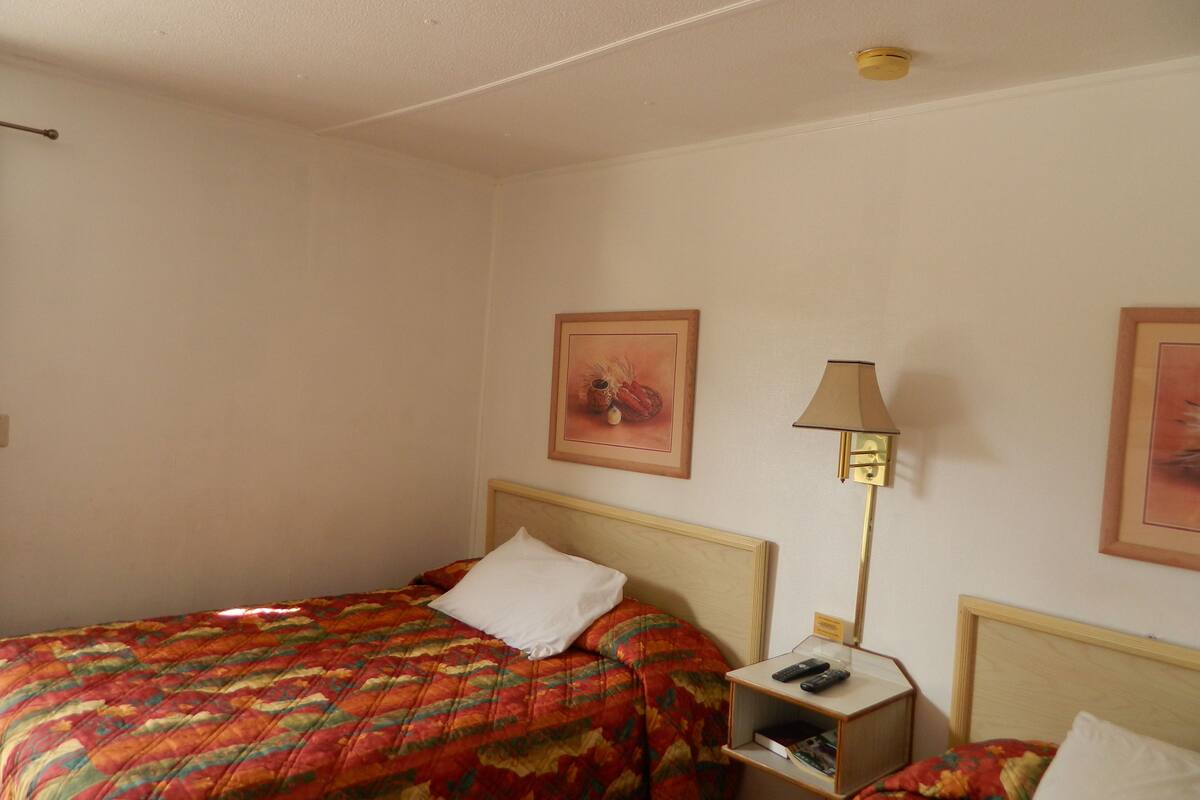 A hotel room with a bed, a bedside table with a lamp, and two framed pictures on the wall.