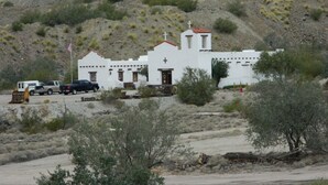 A white church with a bell tower, surrounded by sparse vegetation and parked vehicles. - Marine Motel (Ajo)