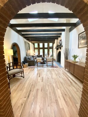 Amplia sala de estar con piso de madera, chimenea y un ventanal grande.
